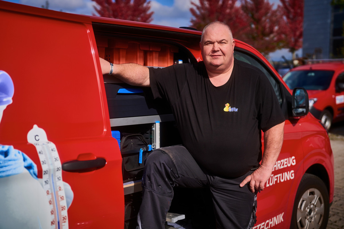 Monteur des Unternehmens Fritz in Offenburg lehnt an einem roten Servicefahrzeug für Heizungs- und Klimatechnik.