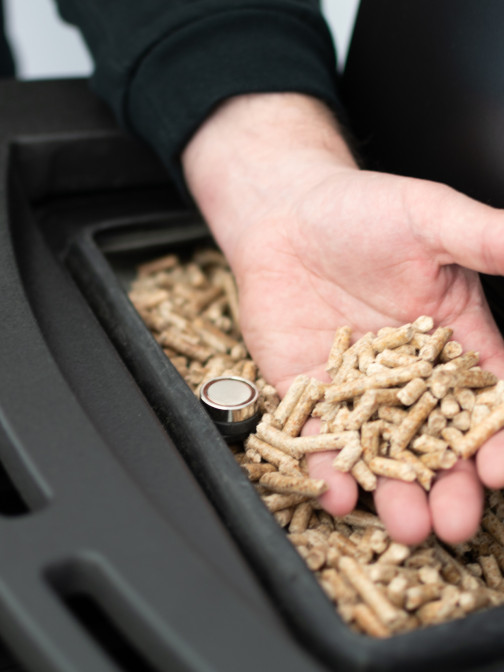 Blick auf eine Person, die eine Hand mit Pellets aus einem Ofen in die Kamera hält.