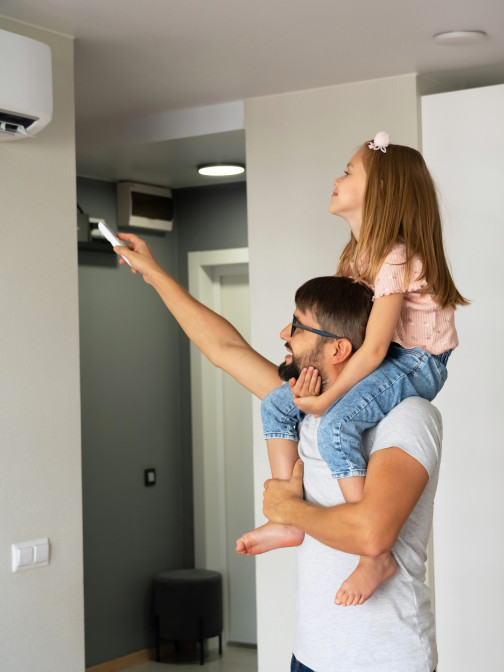 Mann trägt ein junges Mädchen auf den Schultern und hält mit einer Hand die Fernbedienung der Klimaanlage.