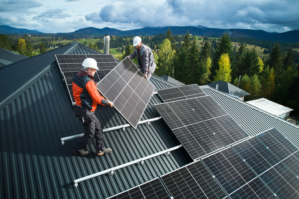 Zwei Arbeiter bringen Solar-Panels  auf einem Dach an.