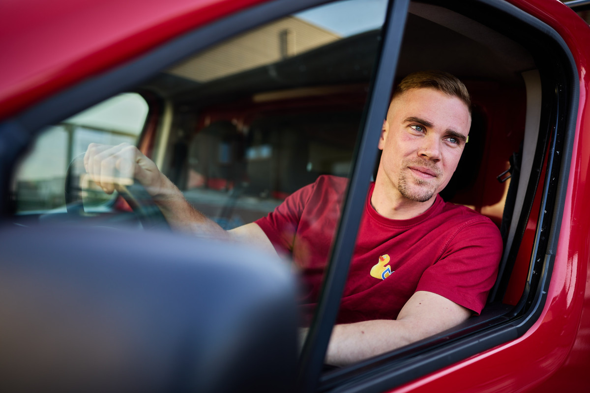 Sebastian Henn sitzt auf dem Fahrersitz des roten fritz-Transporters. Das Fenster ist geöffnet und er lehnt sich leicht hinaus.